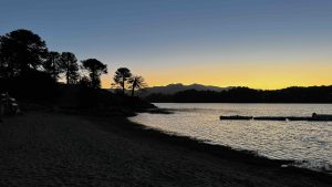 Atardecer en Villa Pehuenia con siluetas de araucarias sobre un cielo ocre y dorado.